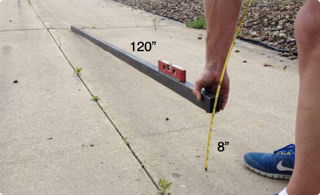 man measuring grade with a level, tape measure, and straight material